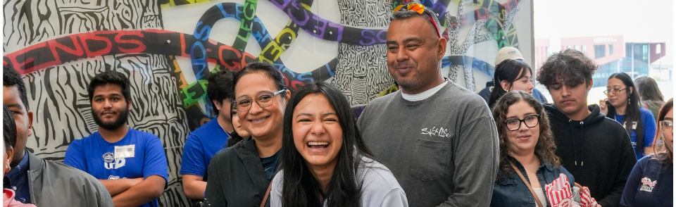Group of smiling students and parents in front of a mural on the UHD cmapus.