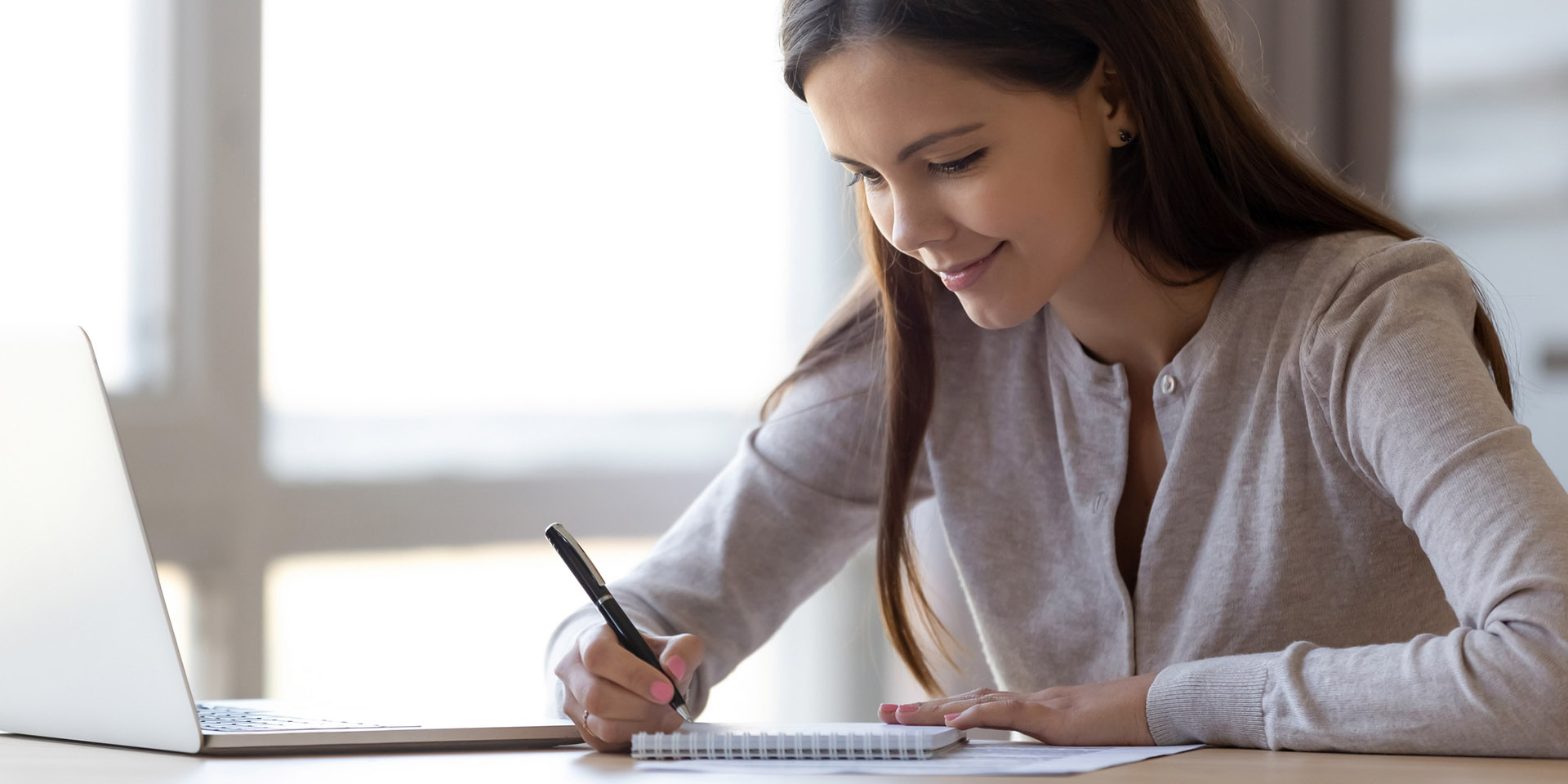 woman writting on a notepad in front of a laptop computer