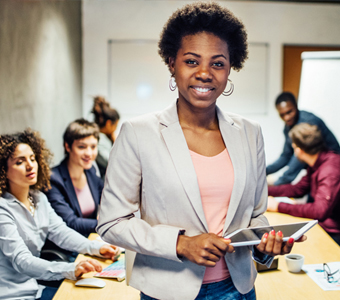 women standing in front of a conference table of people holding a tablet and smiling