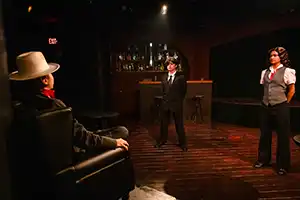 two actors stand facing a seated actor