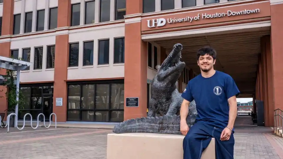 Male student sitting outside with statue of gator mascot