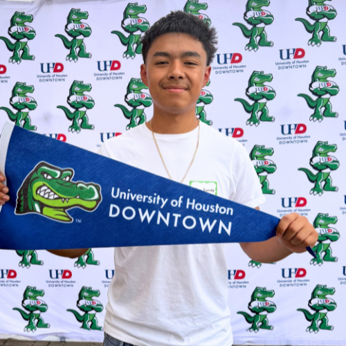 A houston independent school district senior holds up a university of houston-downtown penant in front of a UHD branded step and repeat the university's commitment day 