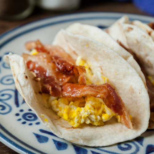 Two egg and bacon breakfast tacos on a patterned plate