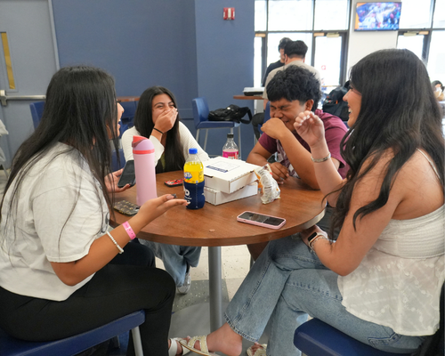 Four students laugh and talk at a table in the university of houston-downtown food court