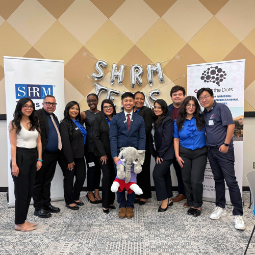 University of Houston Downtown students in the university's chapter of the Society for Human Resources Management smile with faculty advisor at the Marilyn Davies College of Business in Downtown Houston. Balloons behind the group read 