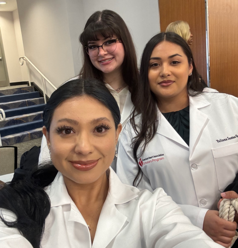 University of Houston-Downtown students Ashley Espinoza, Yuliana Santos Ventura, and Zara Usman smile in American Heart Association Scholars Program white coats at a research presentation.