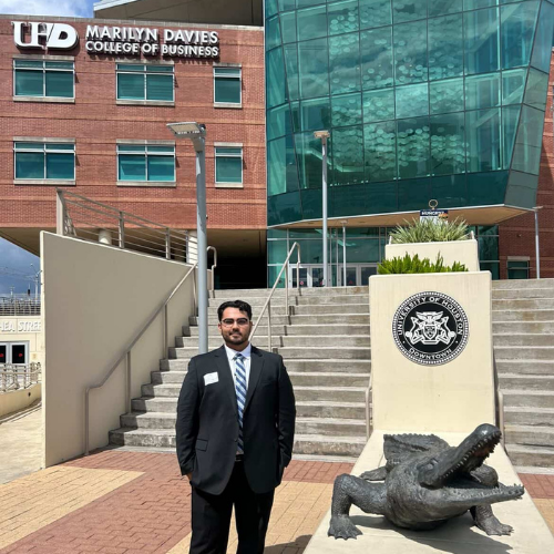 Joe Perez Jr. stands aside an alligator statue at the marilyn davies college of business at the university of houston-downtown