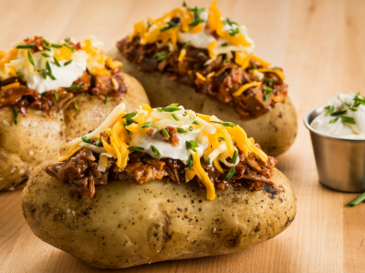 Three baked potatoes loaded with sour cream, cheese, bacon bits, and shredded meat.